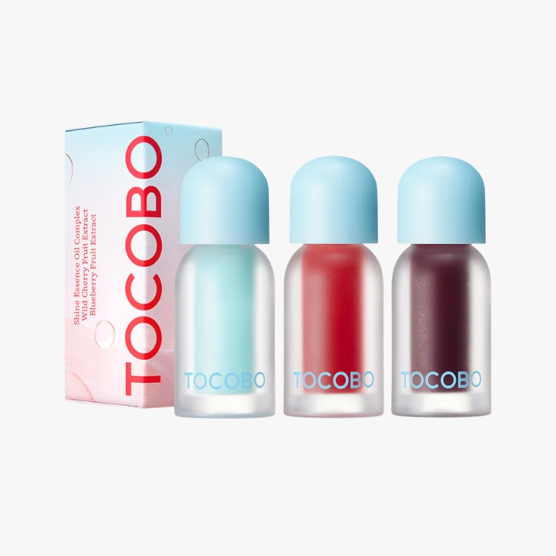 Three TOCOBO cosmetic bottles with blue caps in pastel nail polish shades beside a pink TOCOBO box.