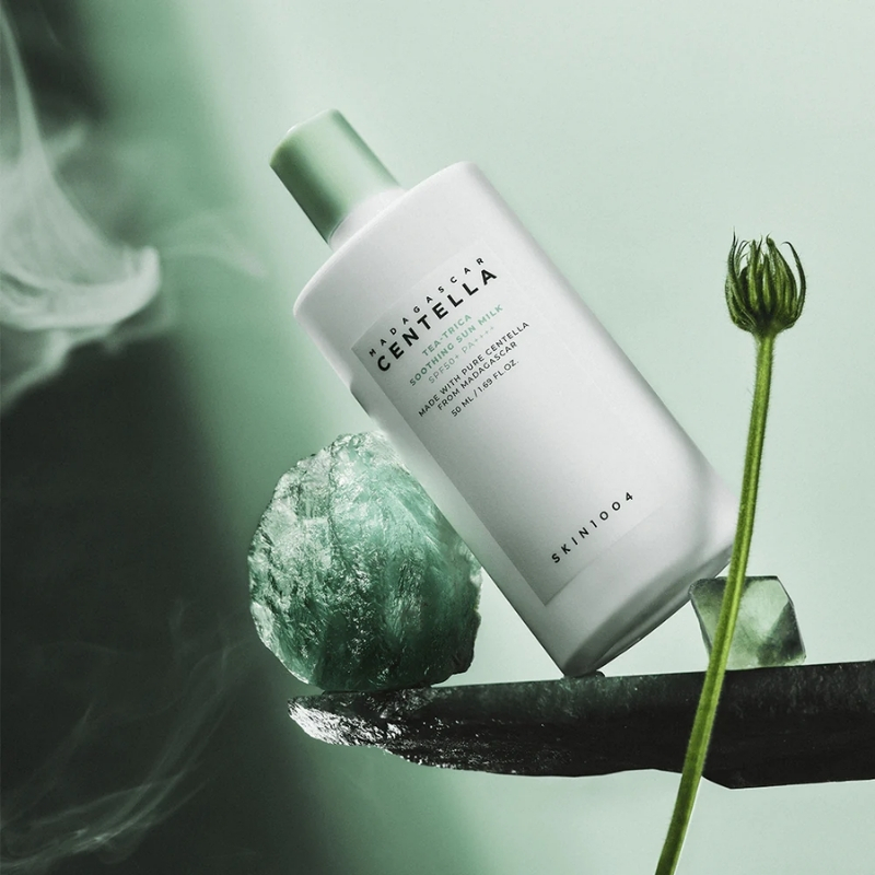 White skincare bottle labeled Centella Soothing Milk rests on a green rock with a plant stem in a soft green backdrop—product shot for skincare.