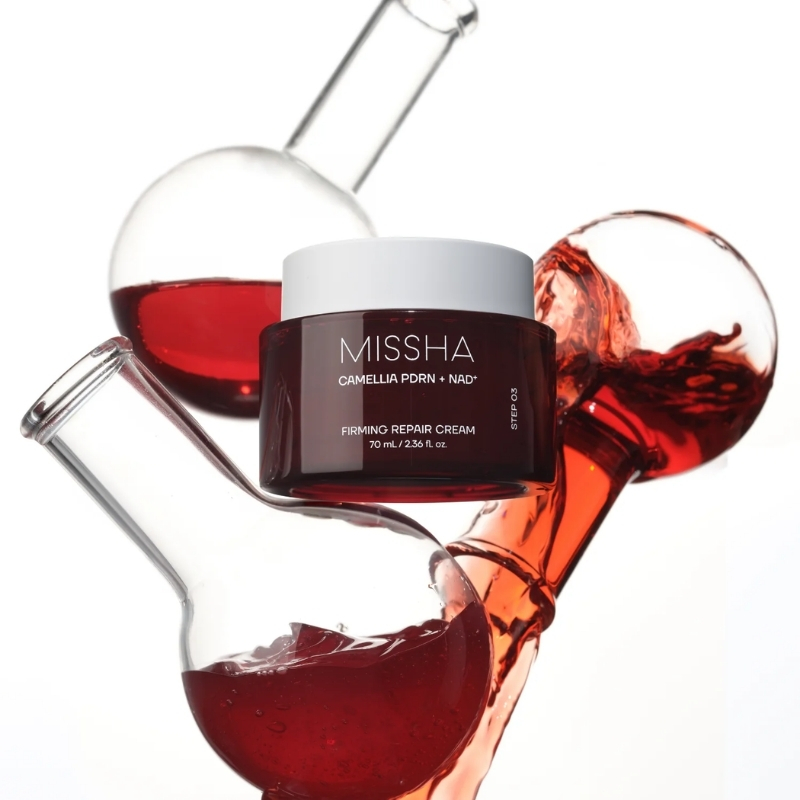 Missha Firming Repair Cream in a burgundy jar, set against red liquid-filled lab glassware in the background.
